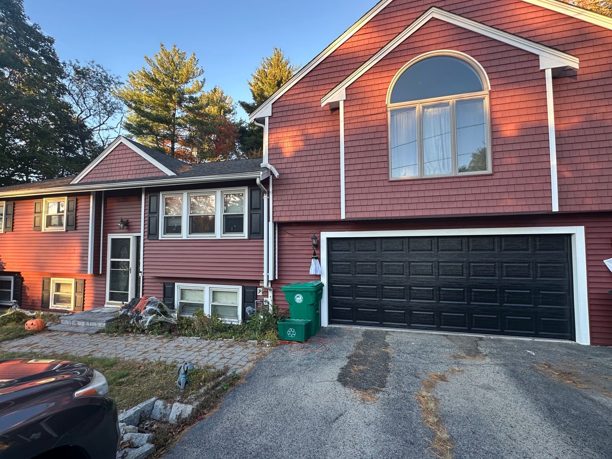 Black raised panel garage door on red colonial home with arched window above